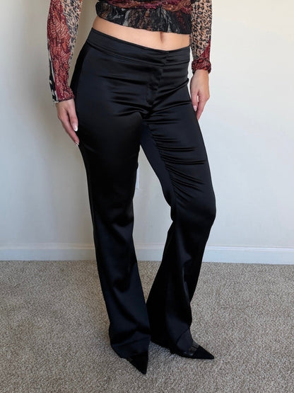 Person wearing black pants and a patterned top against a plain background
