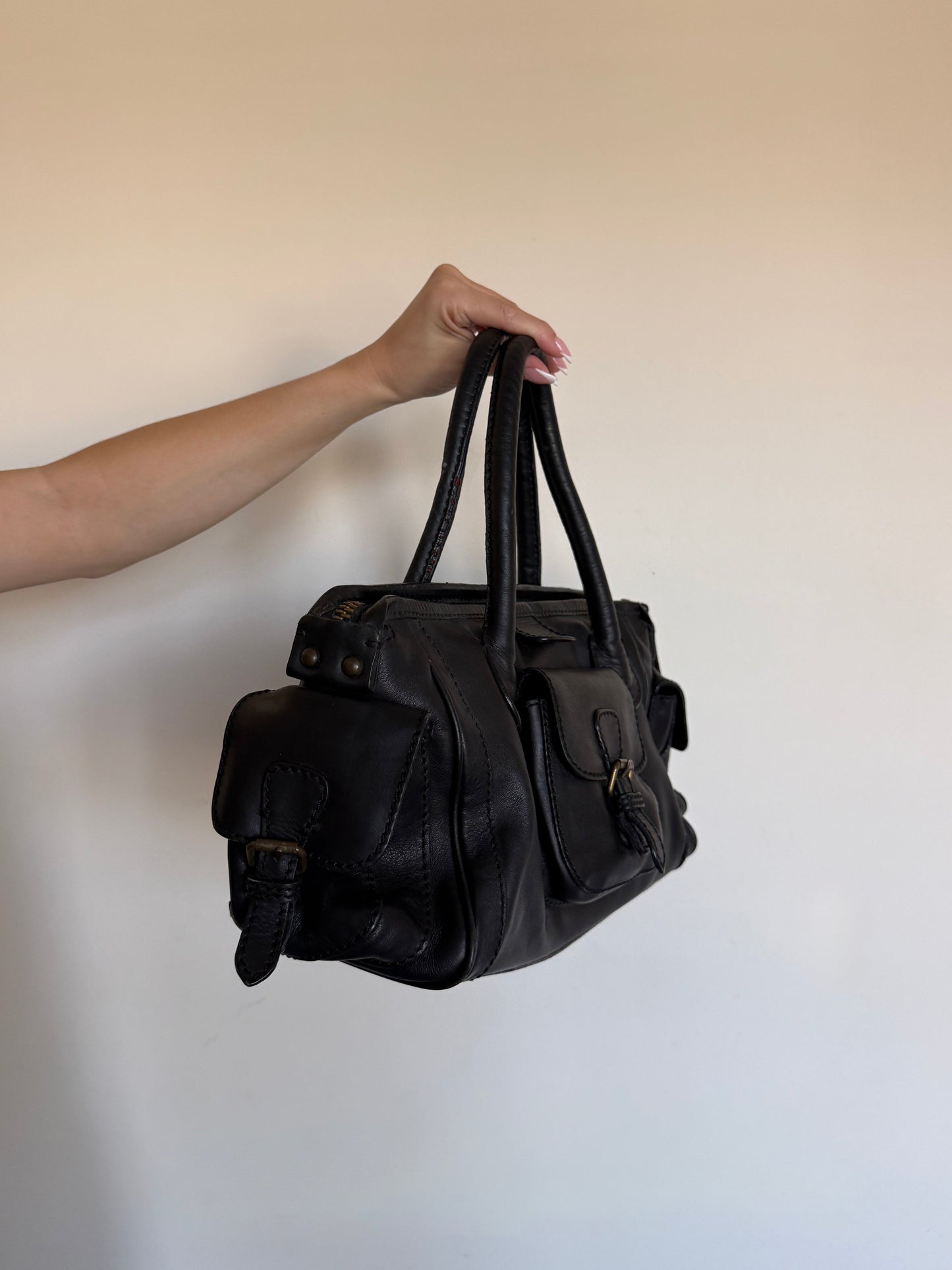 Black leather bag held by a hand against a plain background