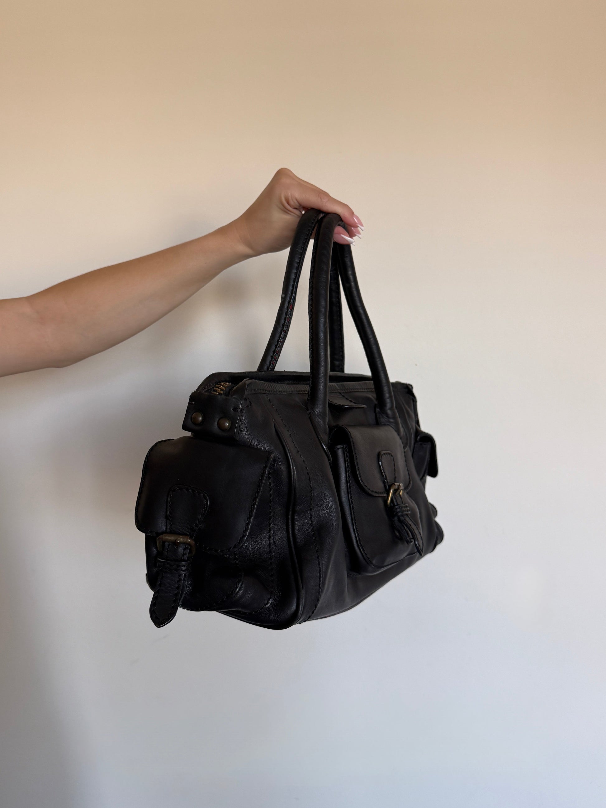 Black leather bag held by a hand against a plain background