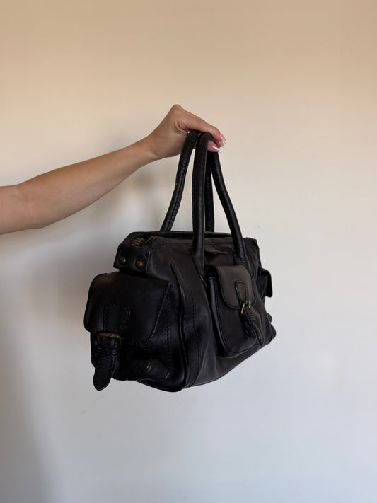 Black leather bag held by a hand against a plain background