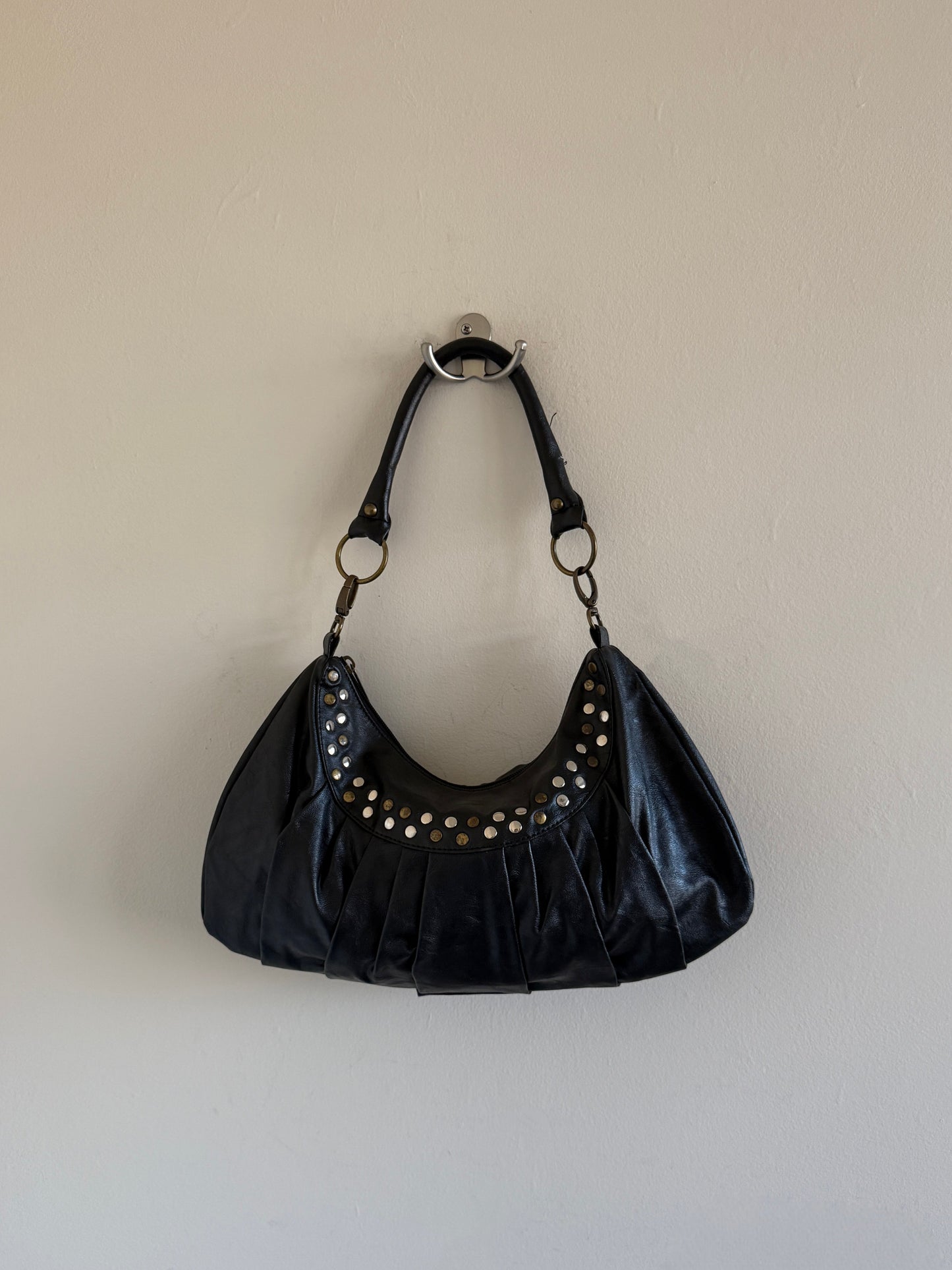 Black handbag with studs on a beige wall