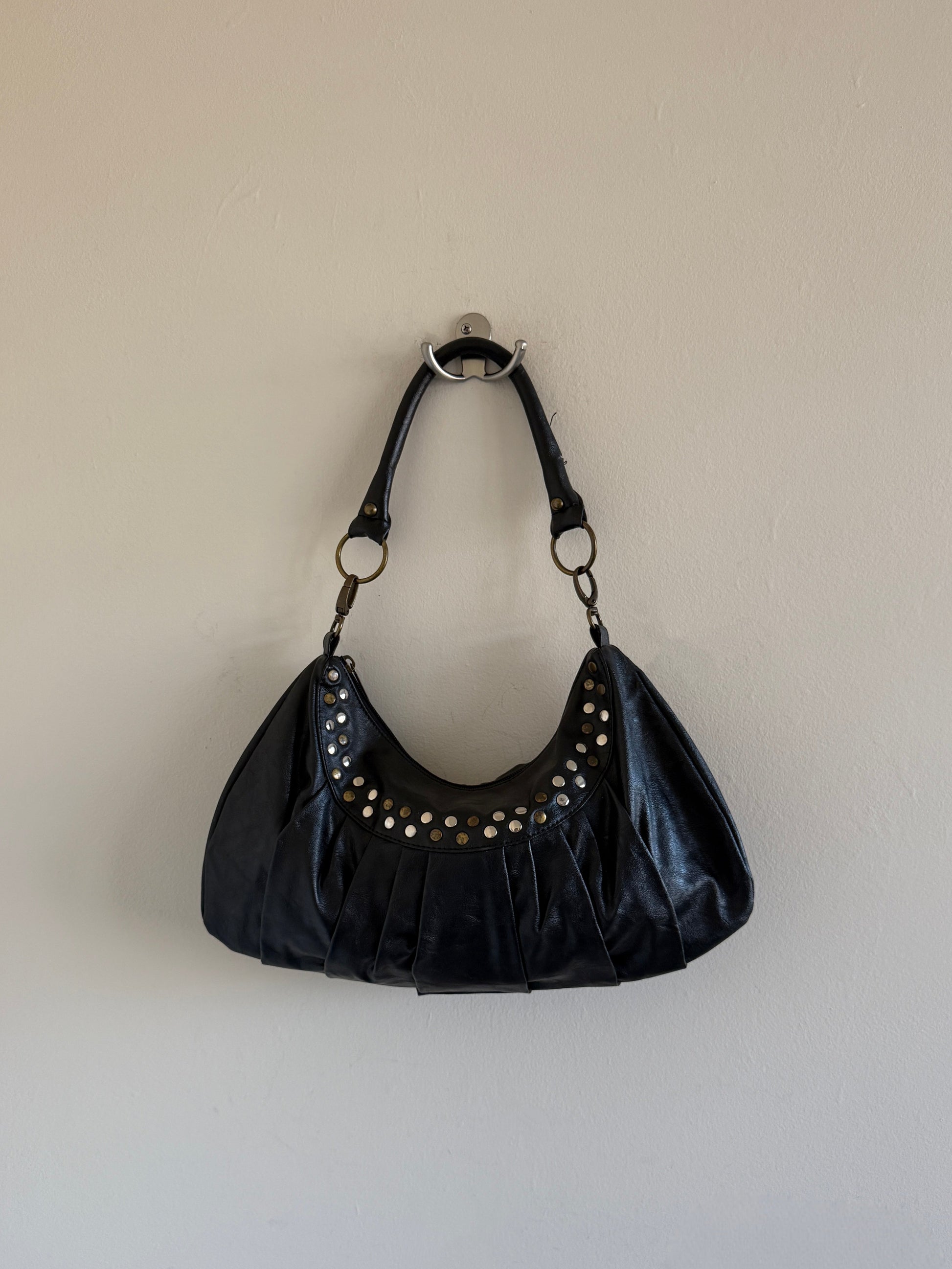 Black handbag with studs on a beige wall