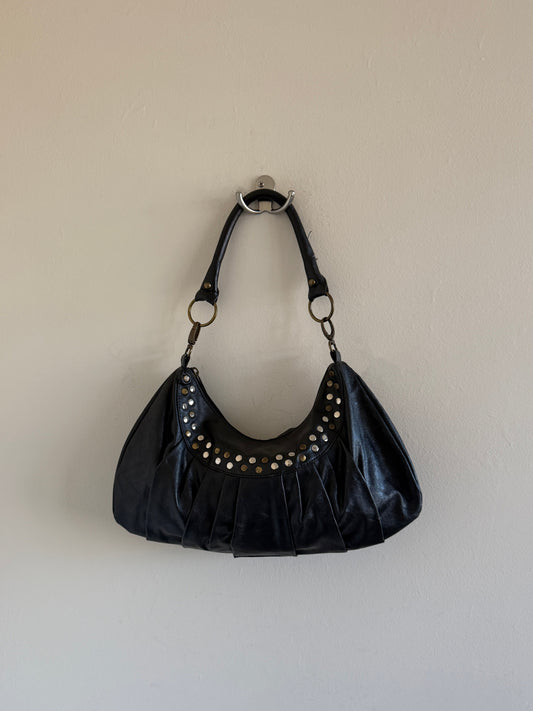 Black handbag with studs on a beige wall