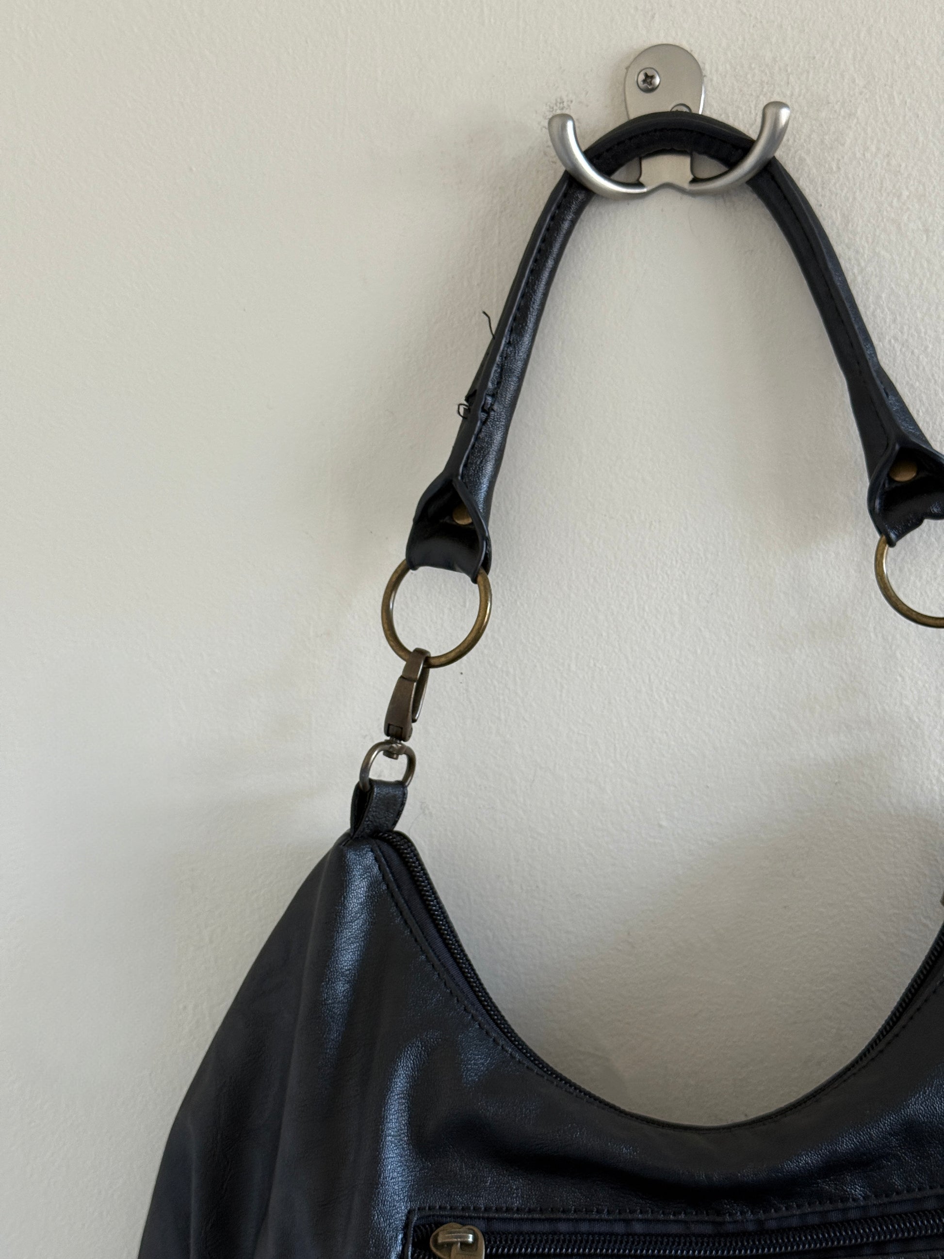 Black leather handbag with a strap hanging on a wall hook against a white background