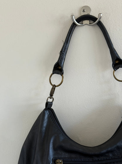 Black leather handbag with a strap hanging on a wall hook against a white background