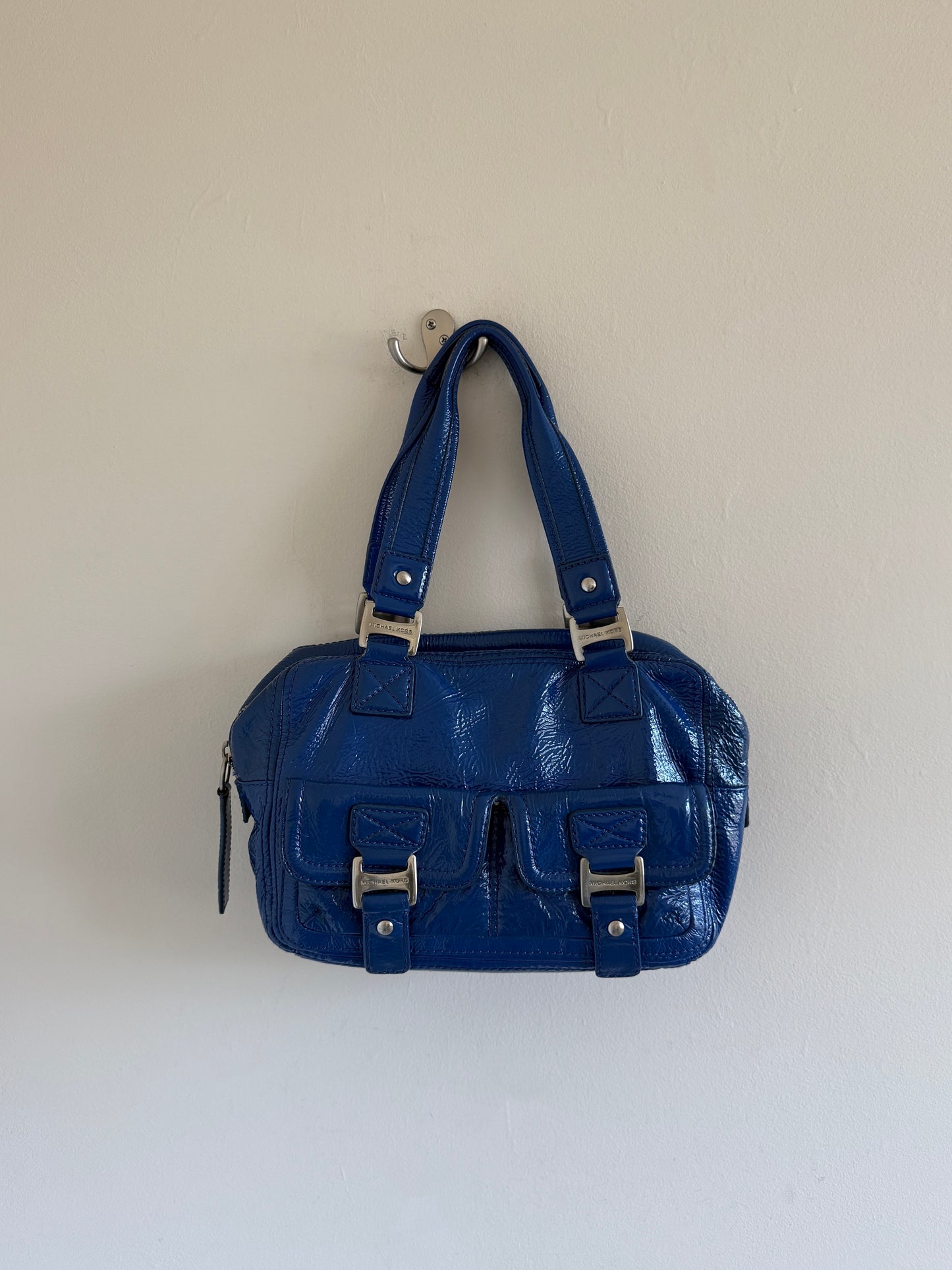 Blue handbag with silver hardware on a white wall