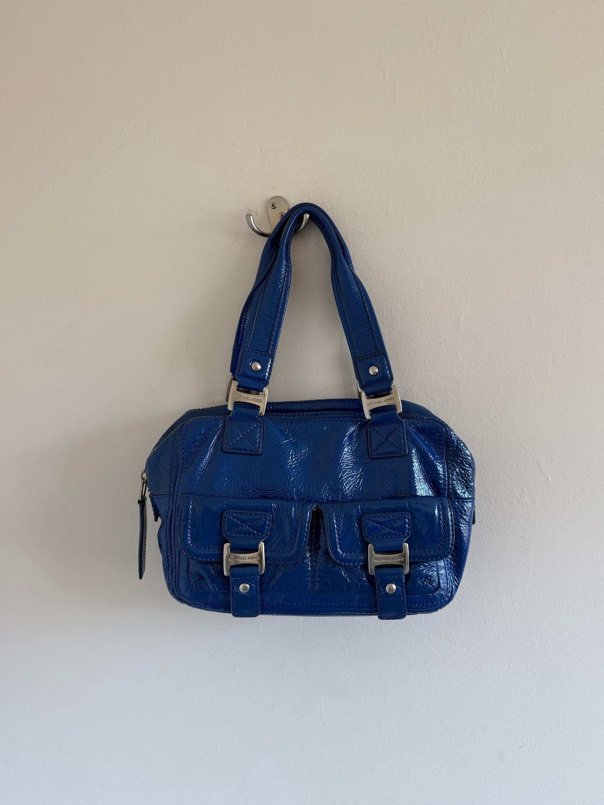 Blue handbag with silver hardware on a white wall