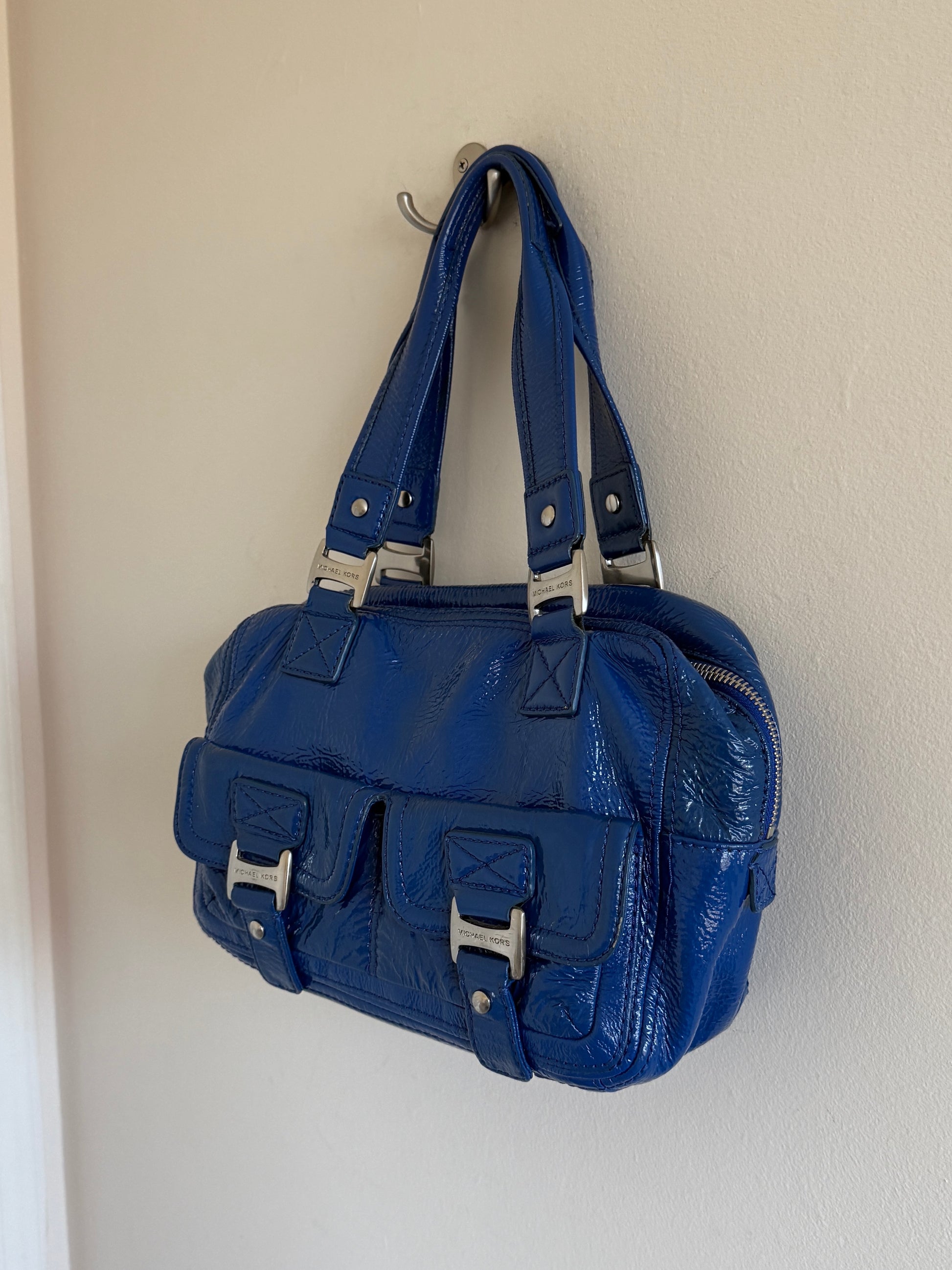 Blue handbag hanging on a hook against a white wall