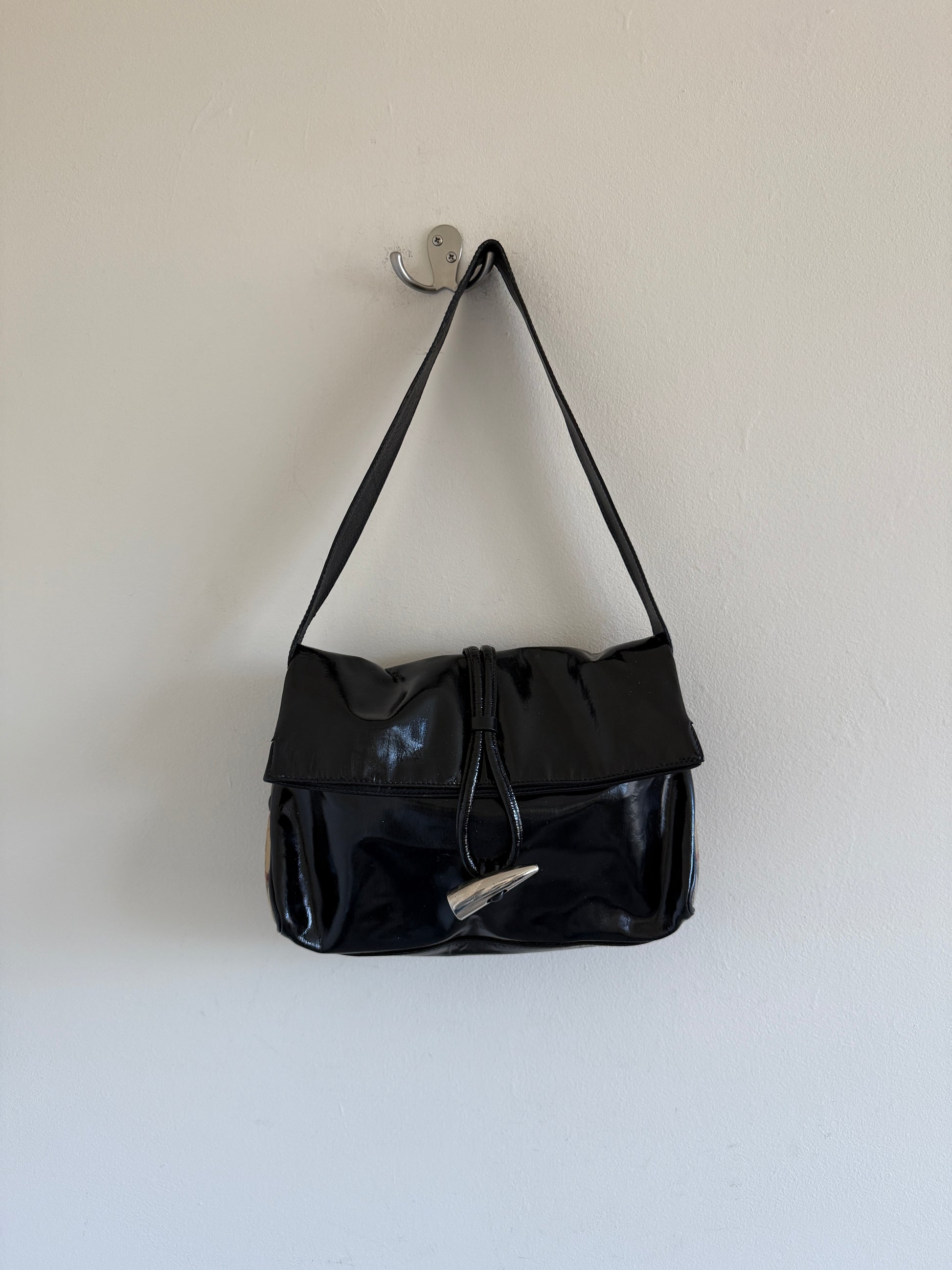 Black handbag hanging on a white wall with a hook.