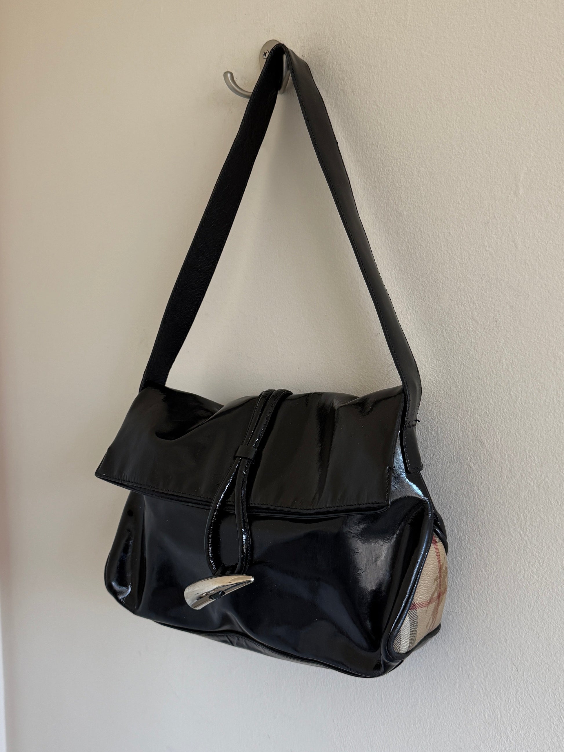 Black handbag hanging on a hook against a white wall