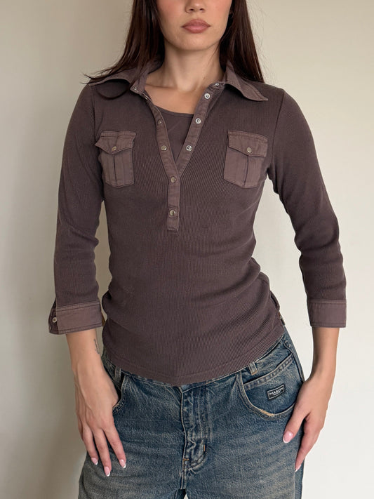 Woman wearing a brown long-sleeve shirt with pocket details against a plain background