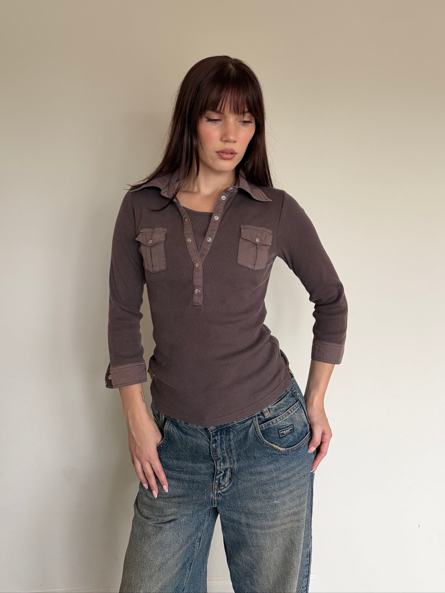Woman wearing a brown long-sleeve shirt and blue jeans against a plain background