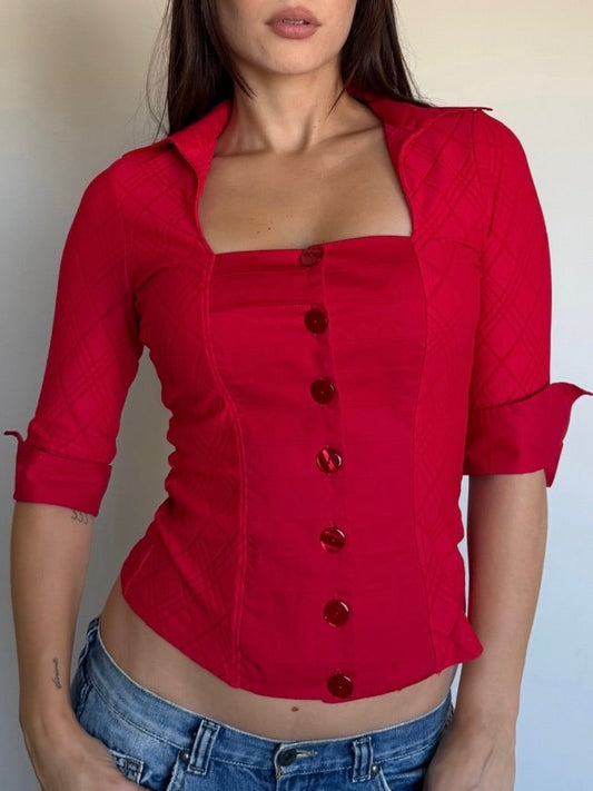 Person wearing a red button-up shirt and blue jeans against a plain background