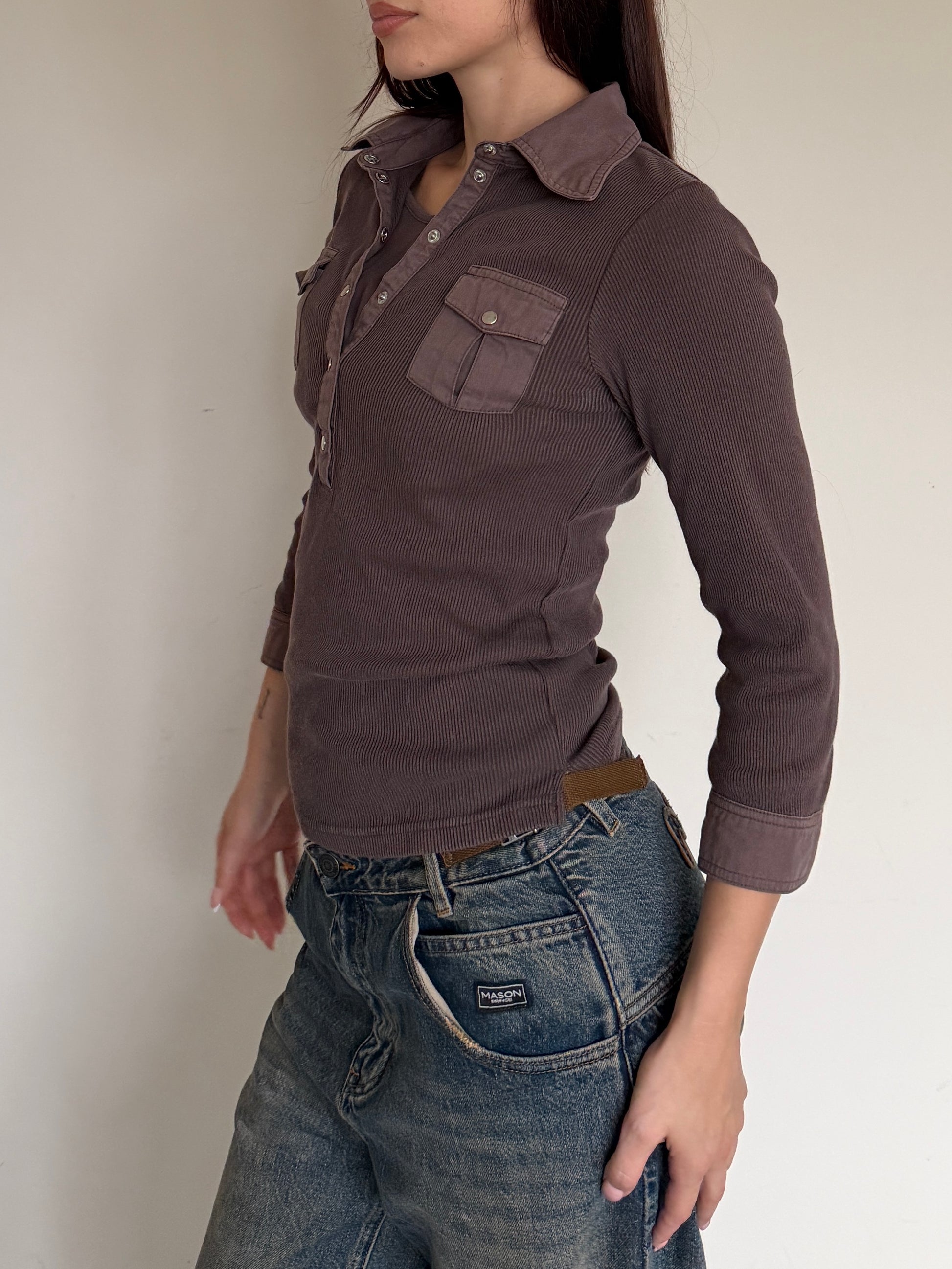 Person wearing a brown long-sleeve shirt and blue jeans against a plain background