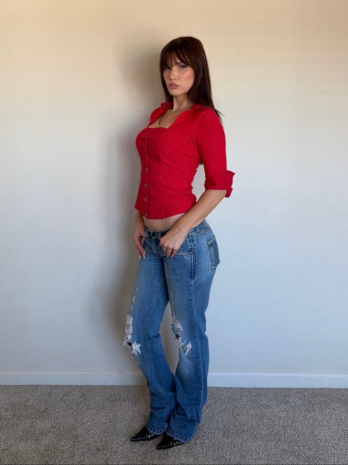 Woman wearing a red top and blue jeans against a plain wall.