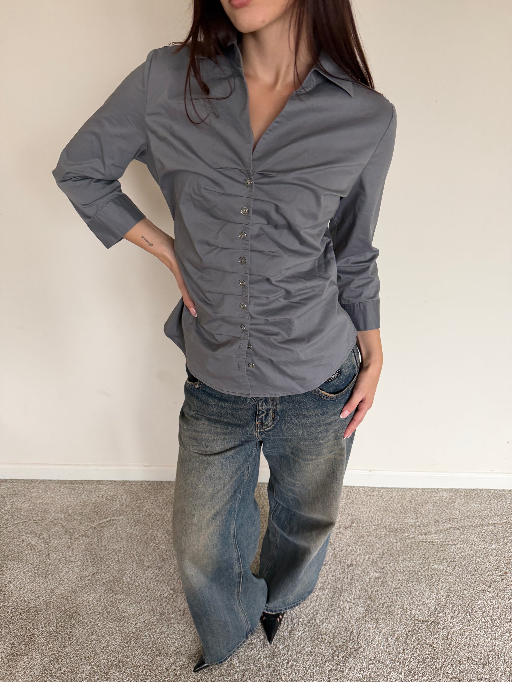 Person wearing a gray button-up shirt and blue jeans against a plain background