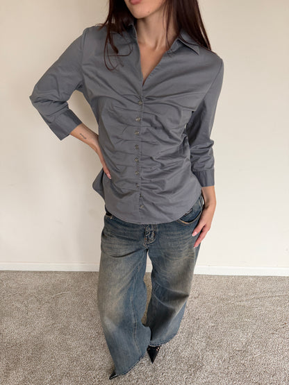 Person wearing a gray button-up shirt and blue jeans against a plain background