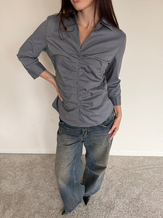 Person wearing a gray button-up shirt and blue jeans against a plain background