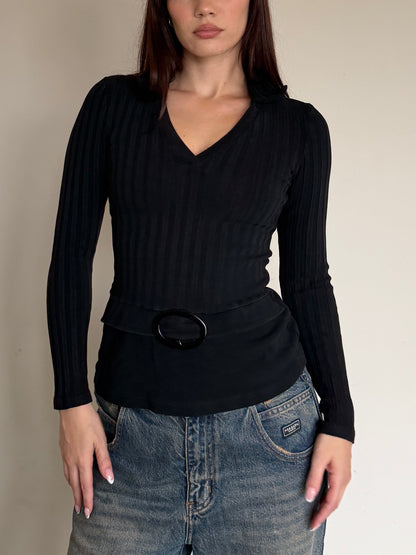 Person wearing a black long-sleeve top and blue jeans against a plain wall.