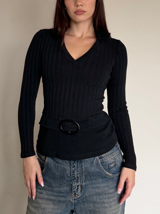 Person wearing a black long-sleeve top and blue jeans against a plain wall.
