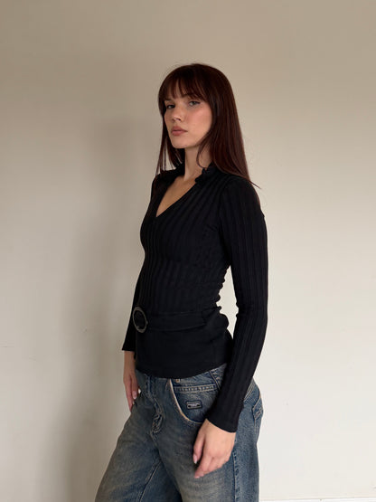 Person wearing a black sweater and blue jeans against a plain wall.