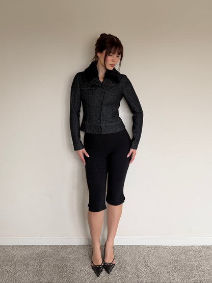 Person wearing a black jacket and black pants against a plain wall.