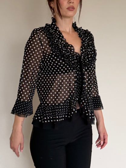 Woman wearing a black polka dot sheer blouse with a plain background
