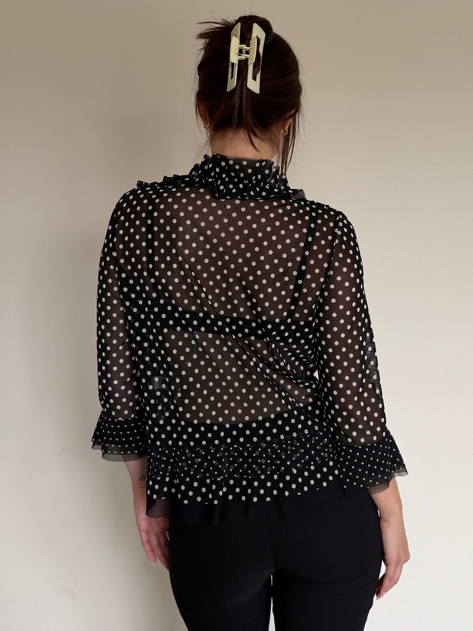Person wearing a black polka dot sheer blouse against a plain background