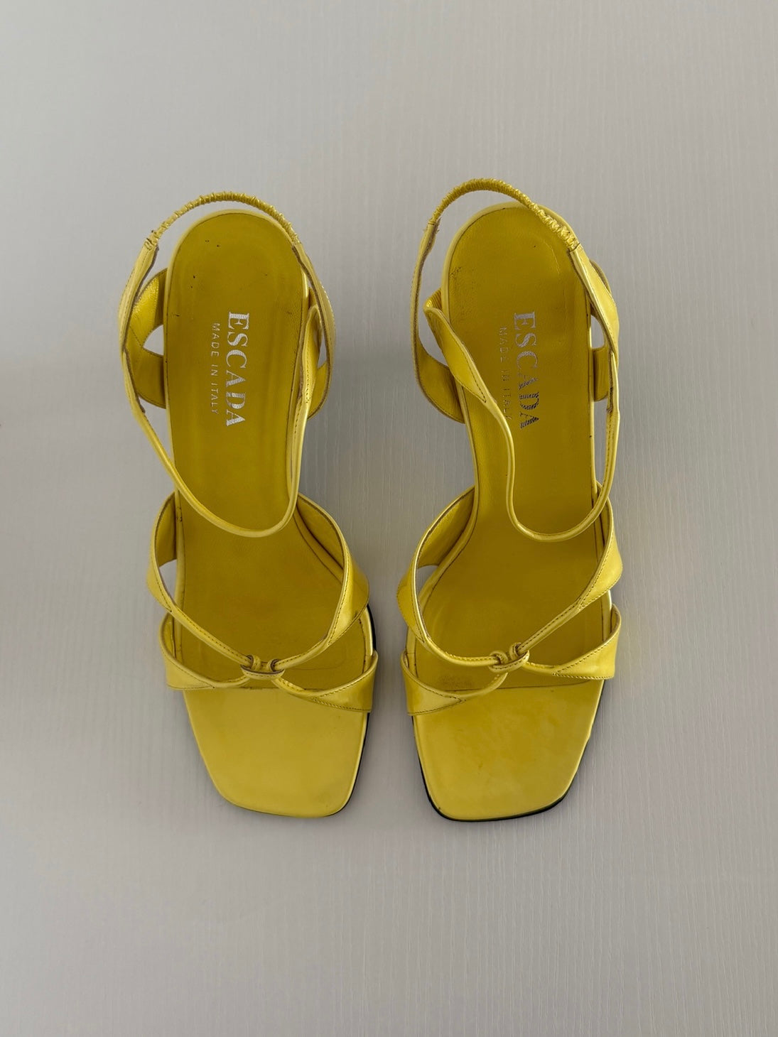 Yellow high-heeled sandals with 'Escada' branding on a light gray background