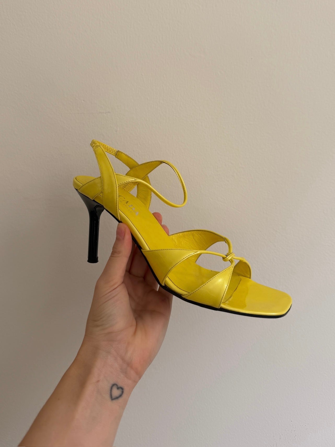 Yellow high-heeled sandal held by a hand against a plain background