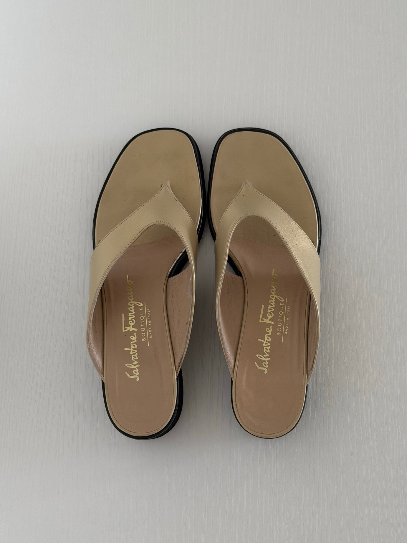 Pair of beige sandals with black soles on a light gray background