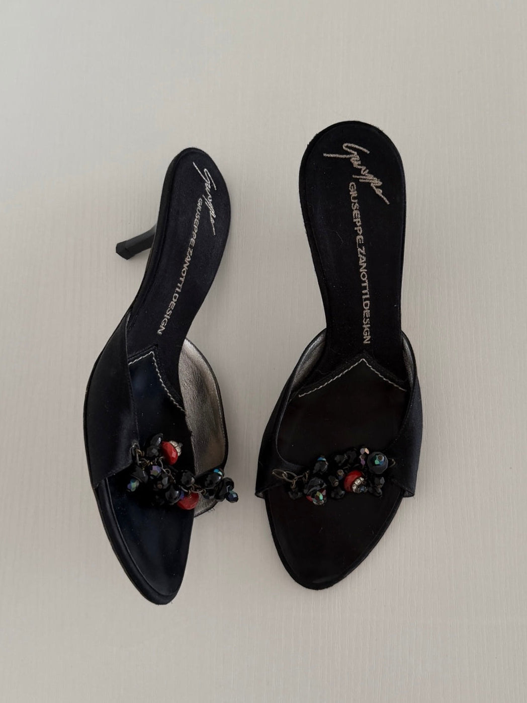 Black high-heeled shoes with embellishments on a light gray background