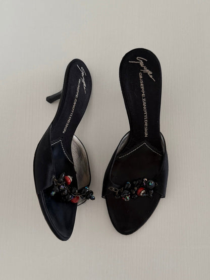 Black high-heeled shoes with embellishments on a light gray background