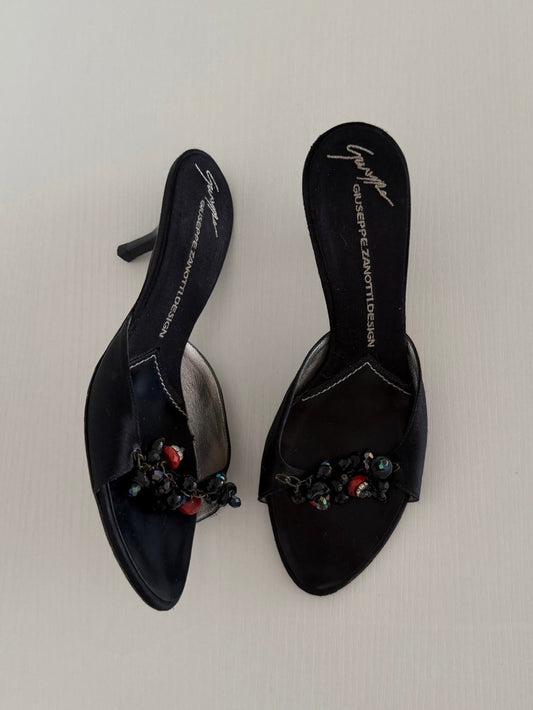 Black high-heeled shoes with embellishments on a light gray background