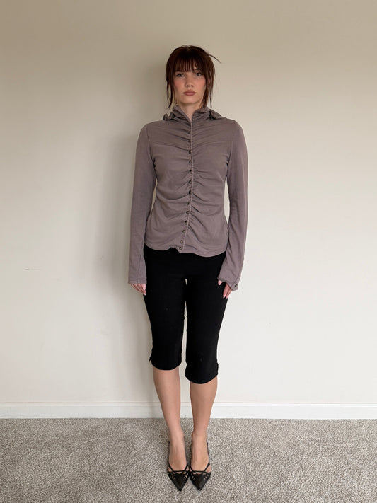 Person wearing a gray blouse and black pants standing against a plain wall.
