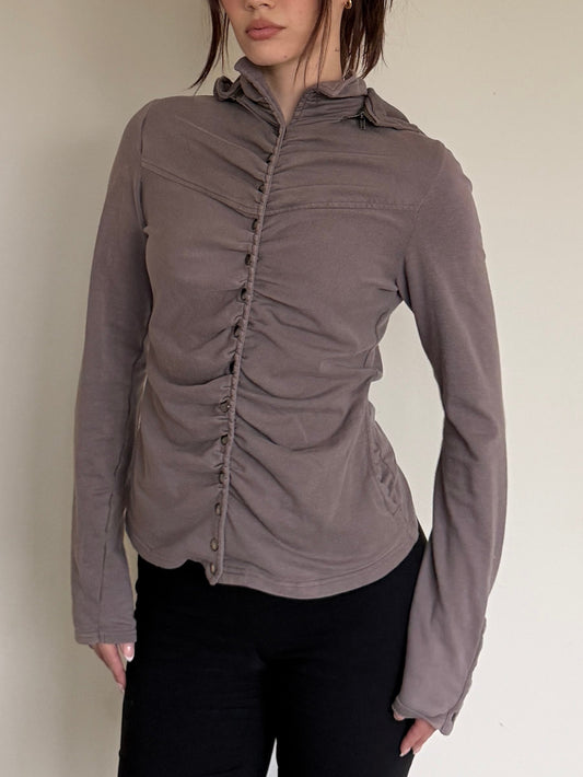 Woman wearing a brown long-sleeve shirt with ruched details against a plain background