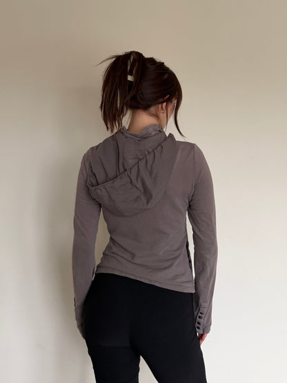 Person wearing a gray hoodie and black pants standing against a plain wall.