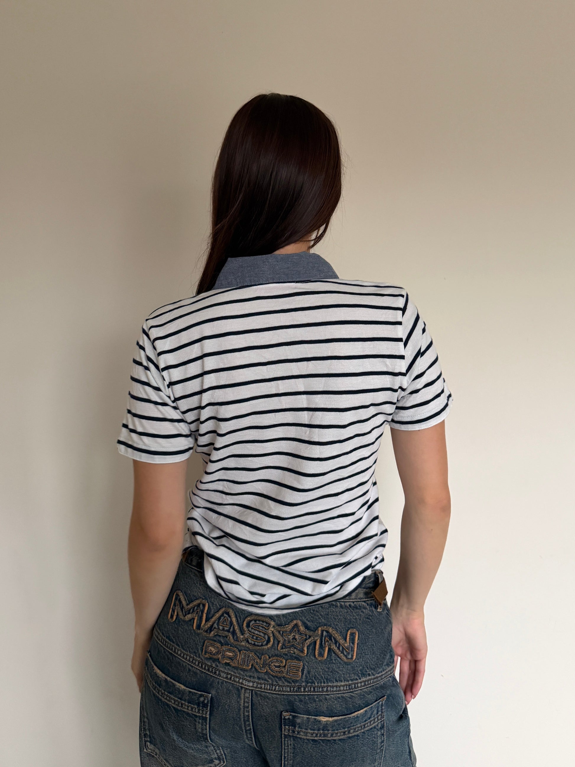 Person wearing a striped shirt and jeans with, standing against a plain background