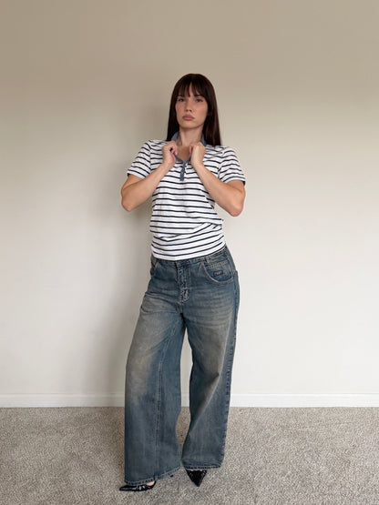Person wearing a striped shirt and wide-leg jeans against a plain wall.