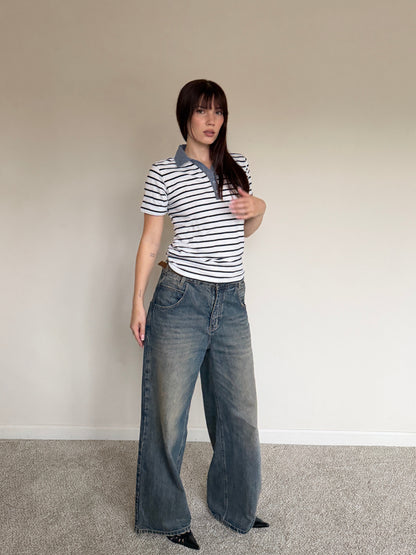Person wearing a striped shirt and wide-leg jeans against a plain wall.