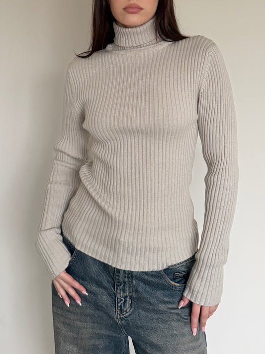Person wearing a beige ribbed sweater and jeans against a plain background