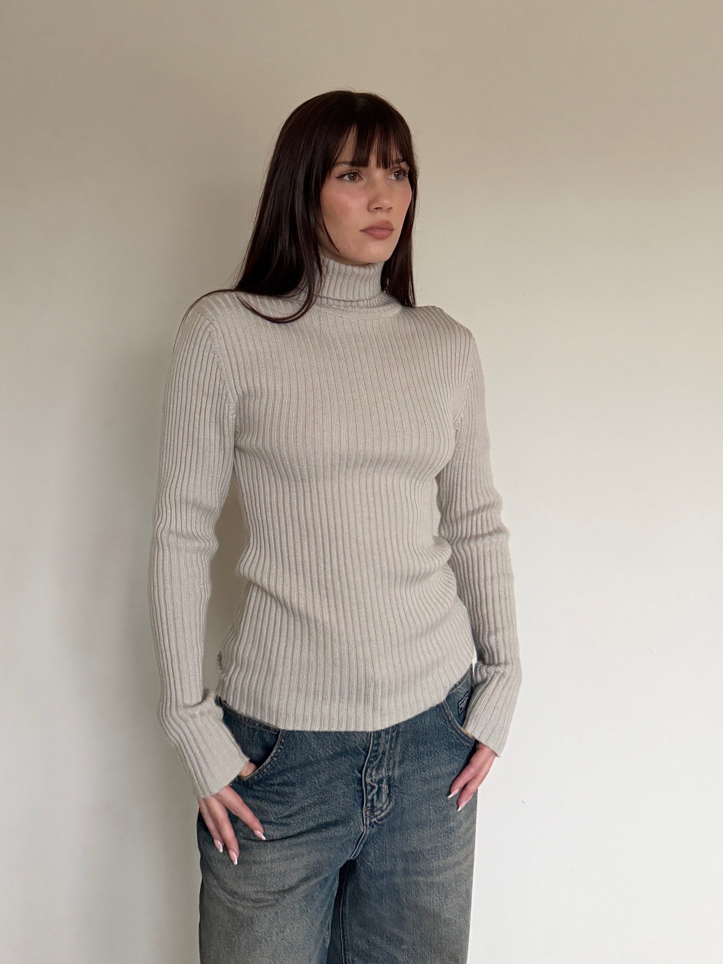 Woman wearing a beige ribbed sweater and jeans against a plain background