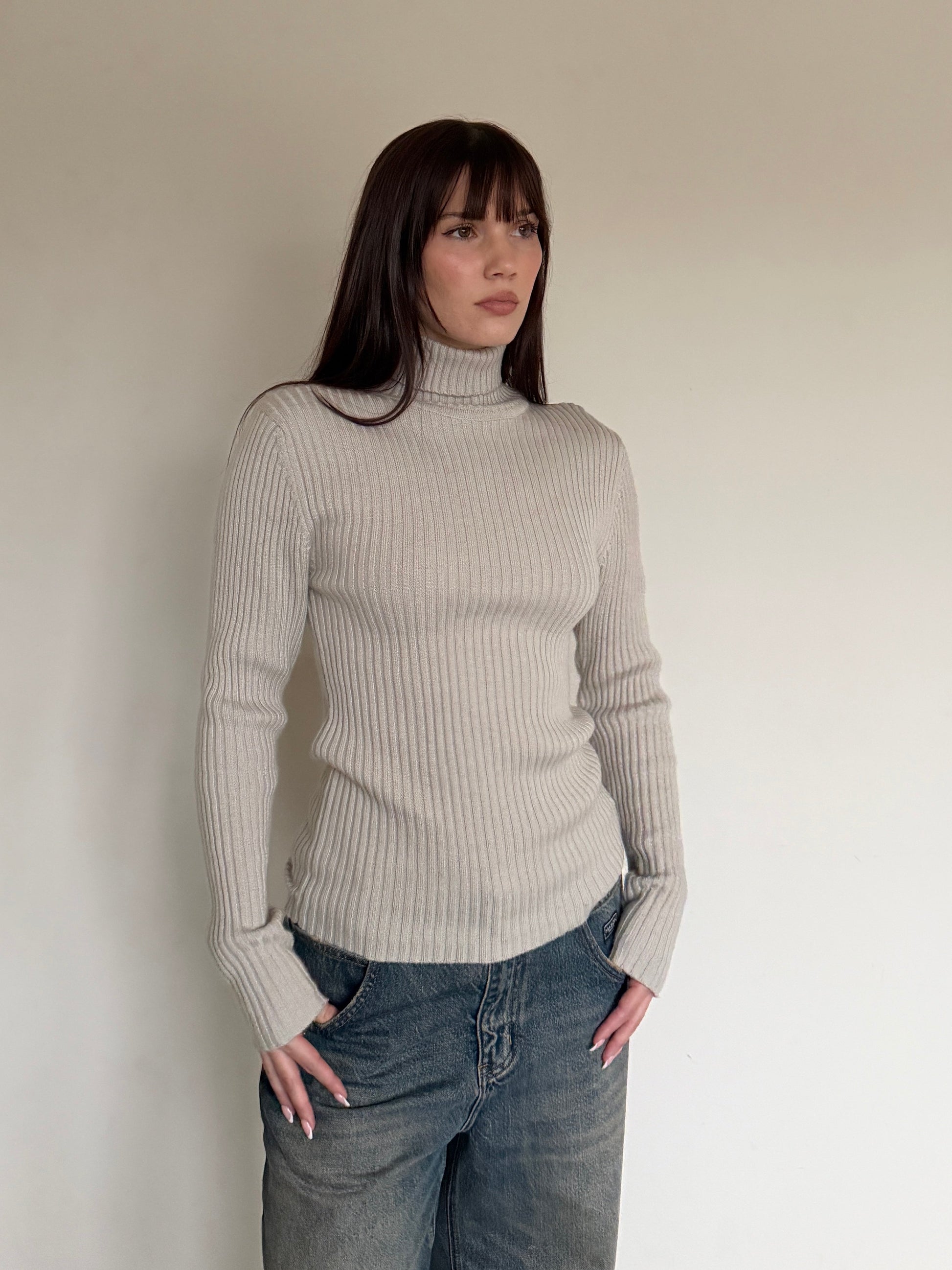Woman wearing a beige ribbed sweater and jeans against a plain background