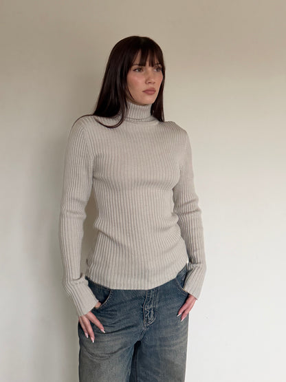 Woman wearing a beige ribbed sweater and jeans against a plain background