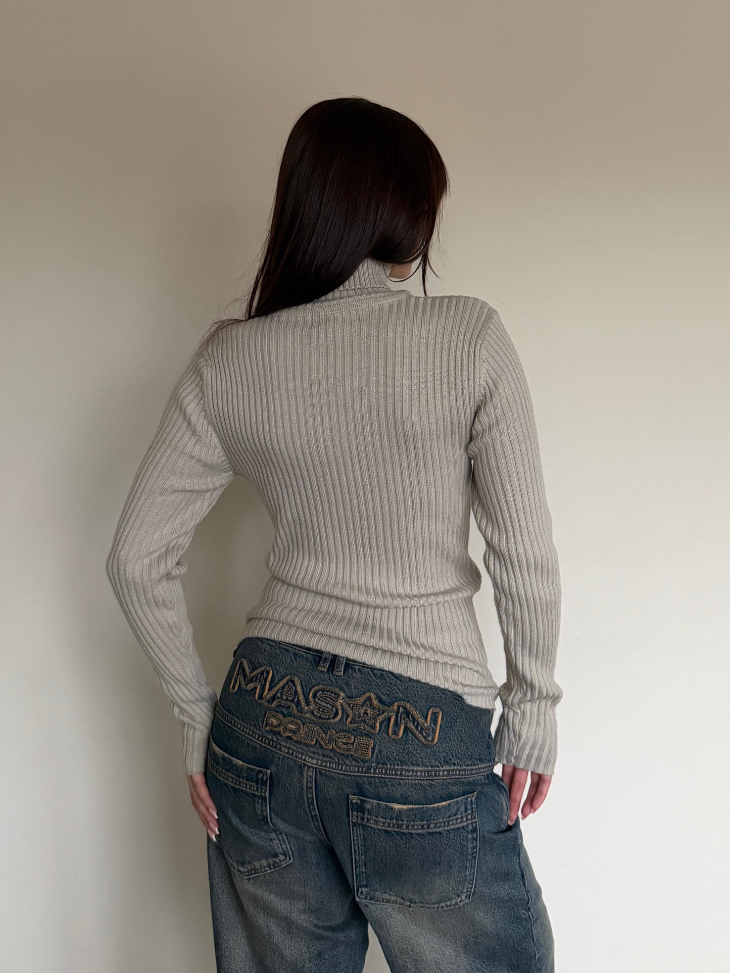 Person wearing a ribbed sweater and jeans with 'Maxim' branding, standing against a plain wall.