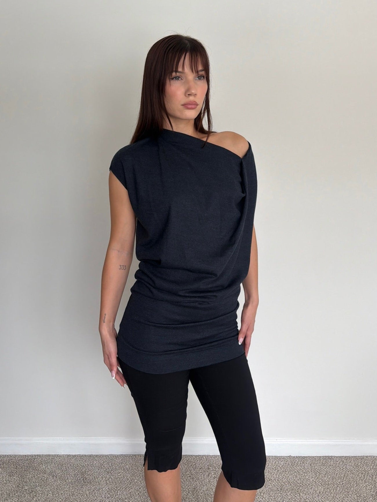Woman wearing a black off-shoulder top and black leggings against a plain background