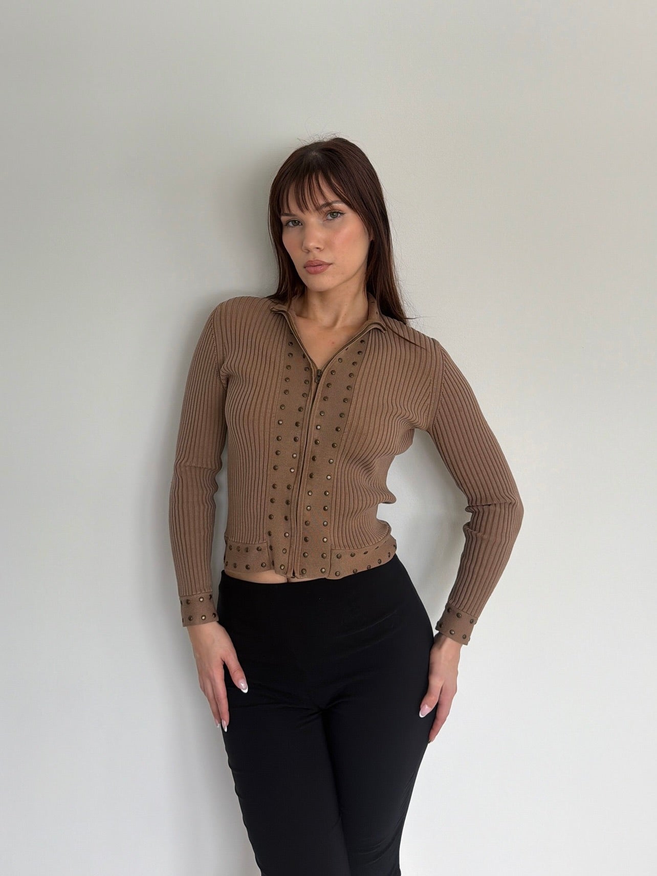 Woman wearing a brown ribbed sweater against a white wall