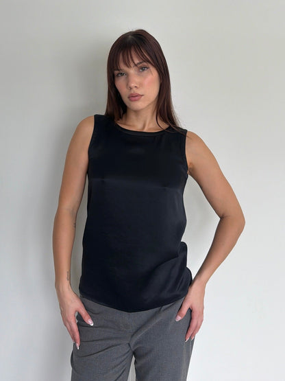 Woman wearing a black sleeveless top and gray pants against a plain background