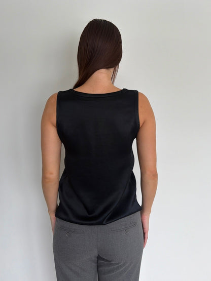 Woman wearing a black sleeveless top and gray pants against a plain background