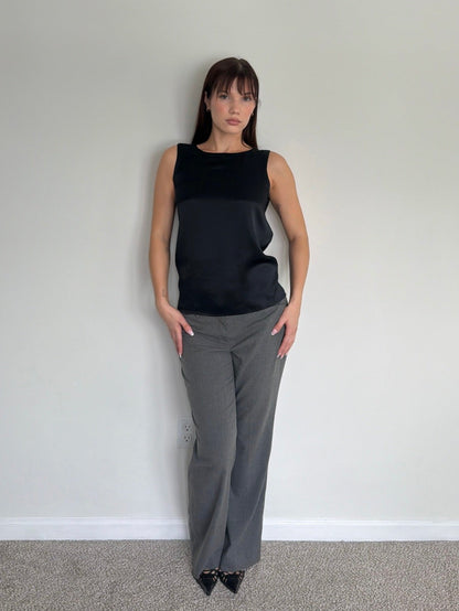 Woman wearing a black sleeveless top and gray pants against a plain white wall.